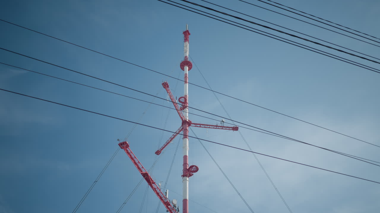 tram moves along snowy urban street towards stop where group of passengers waits beside icy platform, parked cars line roadside, overhead catenary wires stretch across winter sky under soft daylight