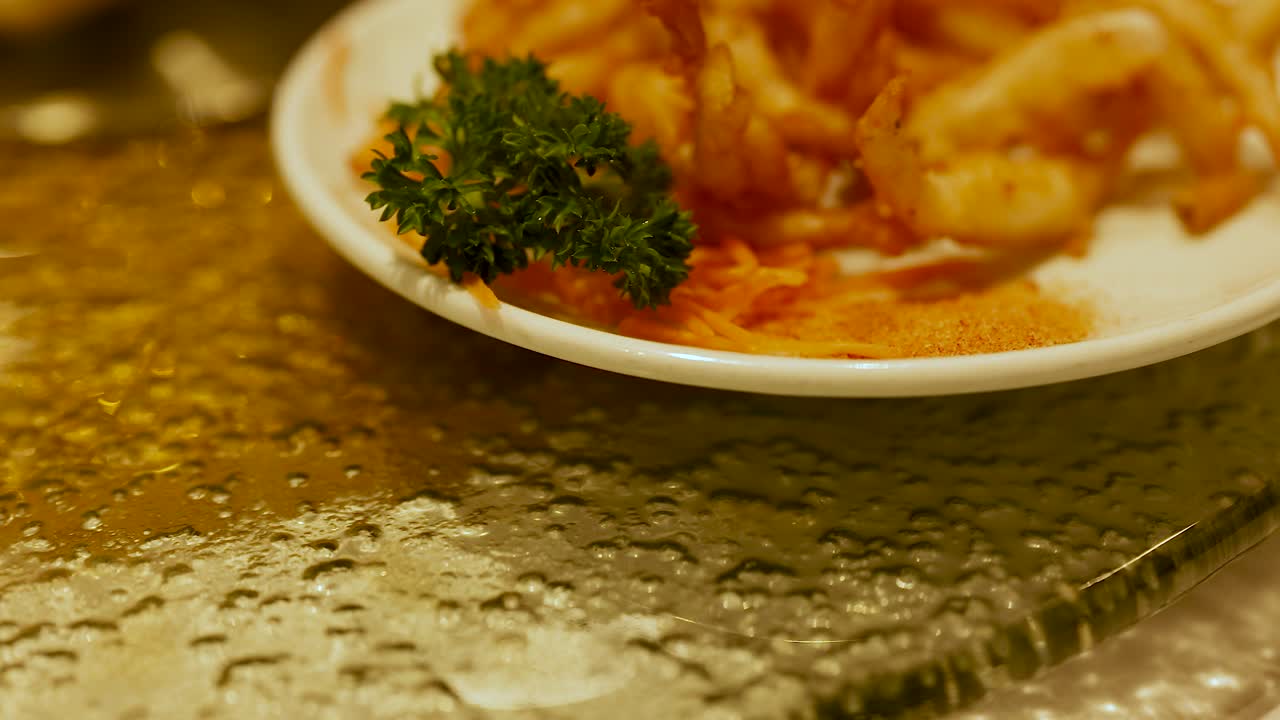 Close-up of deep-fried snacks on a plate with parsley garnish, filmed on a textured glass table in warm lighting