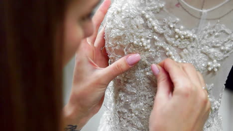 close-up fashion designer for brides in his studio pins needles lace wedding dress. seamstress creates an exclusive wedding dress. secure with pins and needles outline. small private business. sew rhinestones and crystals to the dress thread and needle. jewelry work.