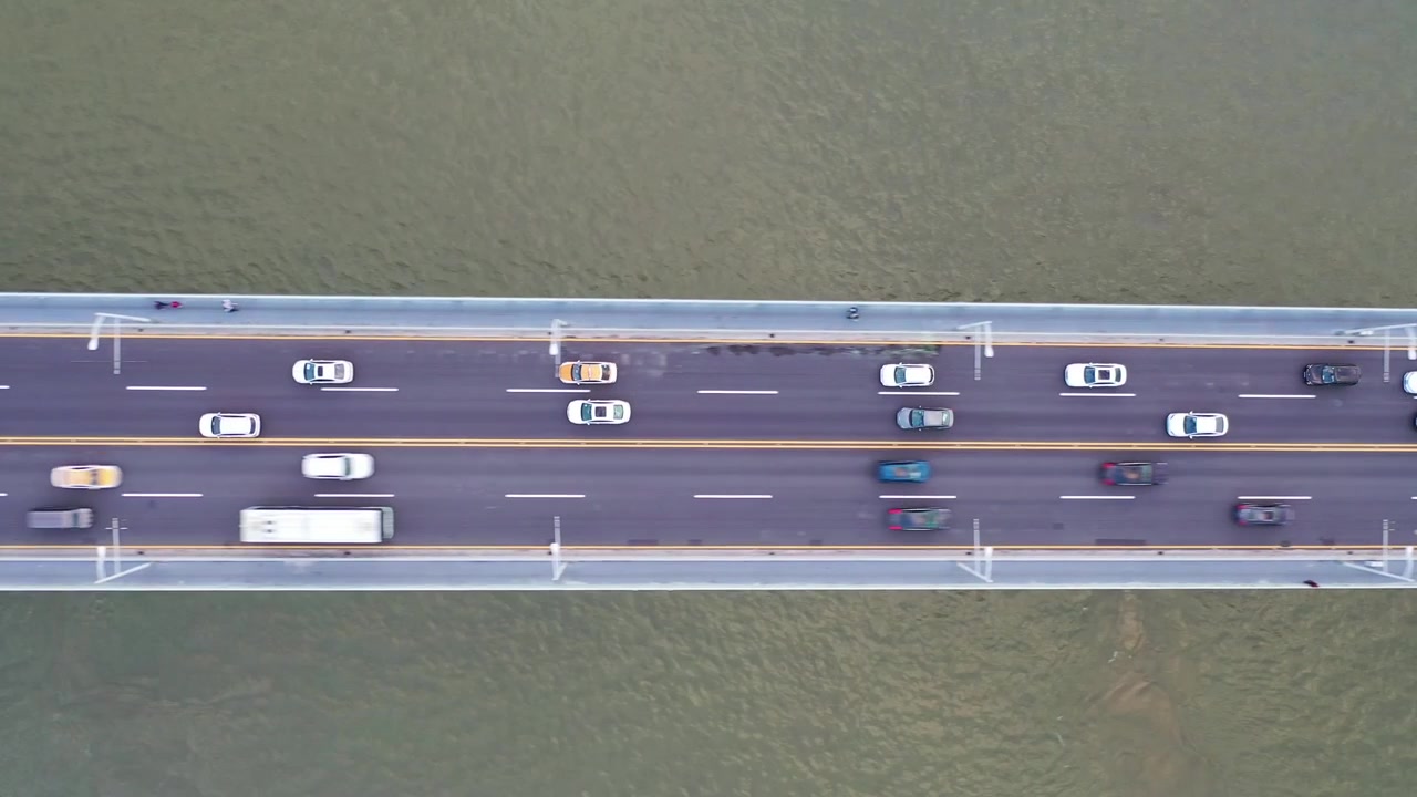 汽車和巴士沿著跨越水面的多車道公路橋行駛的垂直俯瞰空拍圖，突顯日間的城市交通、交通流量和對稱性