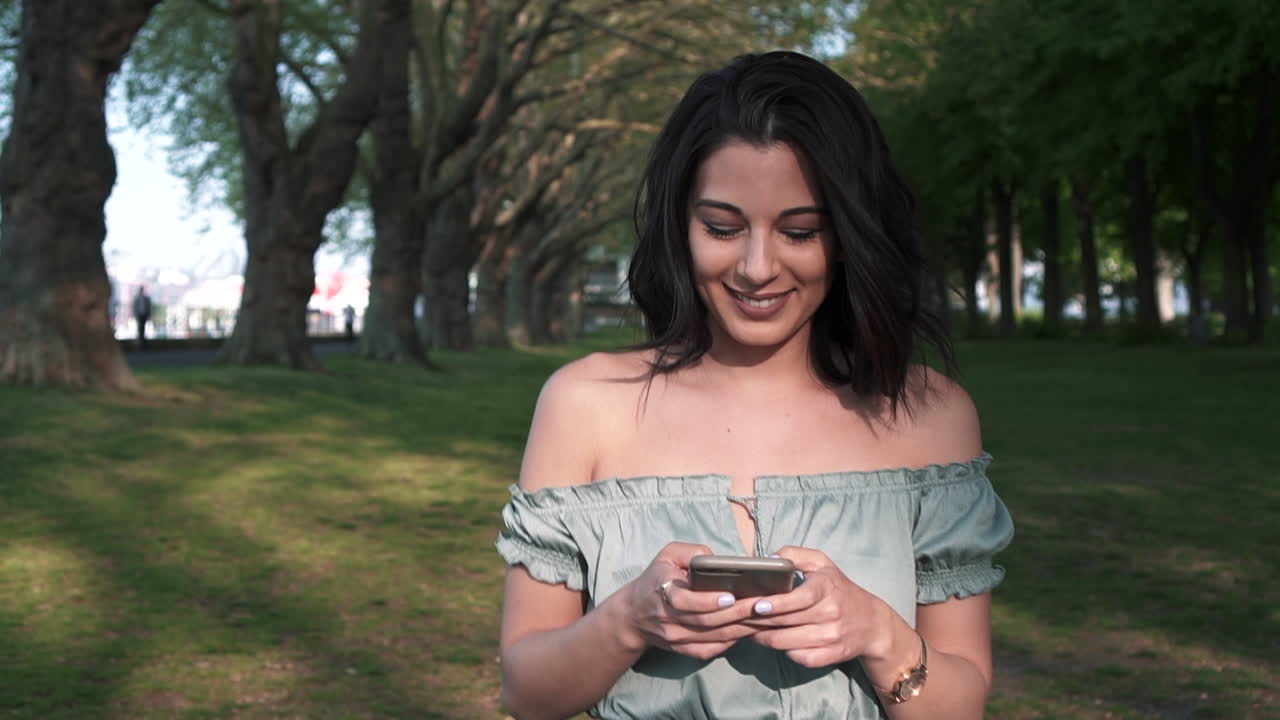 joven morena latina confiada y atractiva con un atuendo informal, usa su teléfono inteligente, sonríe alegremente a los mensajes de texto, mira a su alrededor