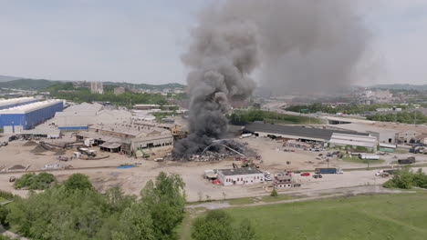 Imágenes-Aéreas-Estáticas-Y-Centradas-En-Cámara-Lenta-De-Un-Gran-Incendio-De-Chatarra-Con-Servicios-De-Emergencia-Cubriéndolo-Con-Agua-Mientras-El-Humo-Gris-Se-Mueve-Hacia-El-Cielo