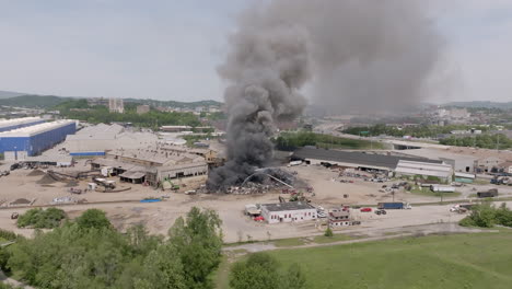 cámara lenta estática y centrada imágenes aéreas de un gran incendio de chatarra de metal con los servicios de emergencia que lo cubren con agua a medida que el humo gris se mueve hacia el cielo