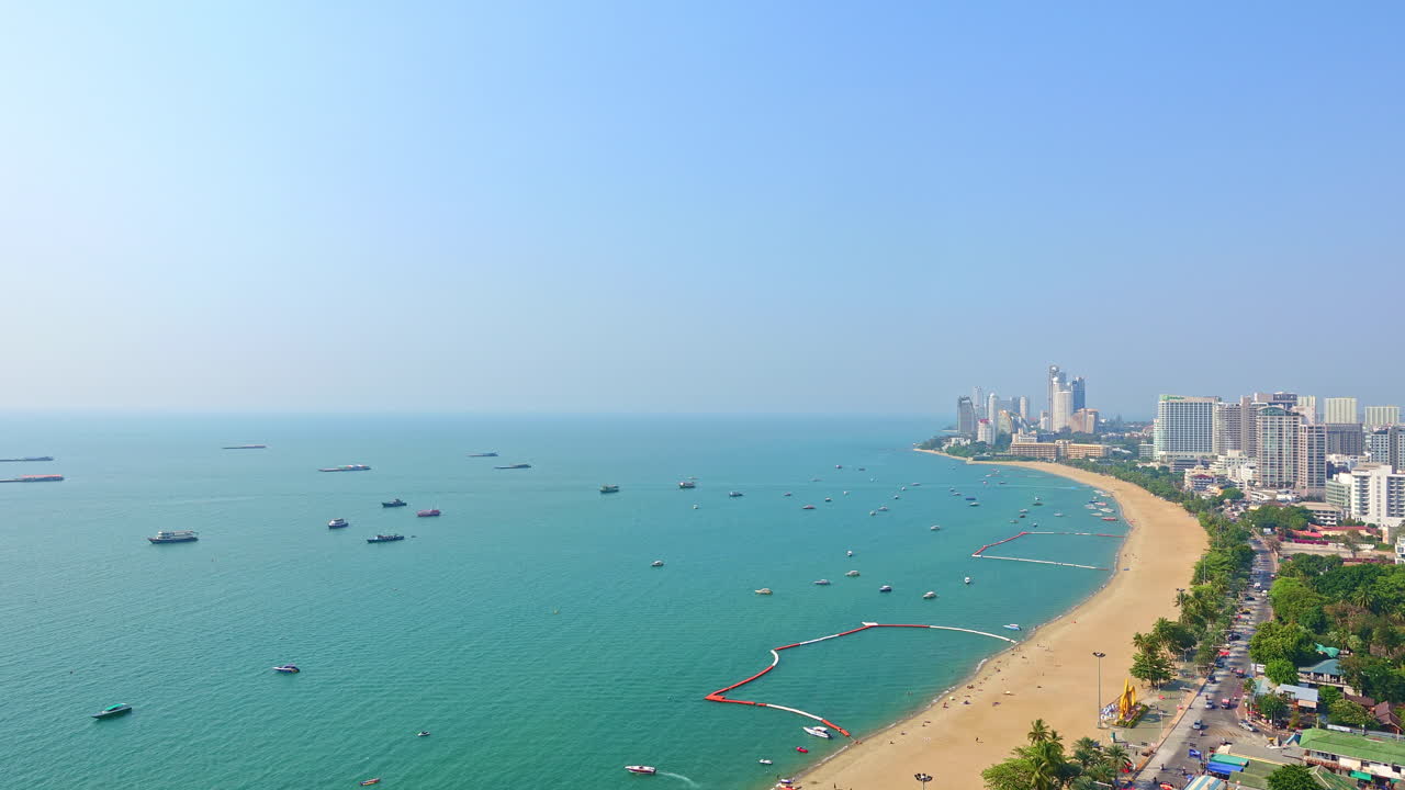 Scenic beauty of Thailand and the wide sandy beach of Pattaya City. Beautiful blue water with boats anchored and cars passing on the coast road. City on ocean shore and popular tourist destination