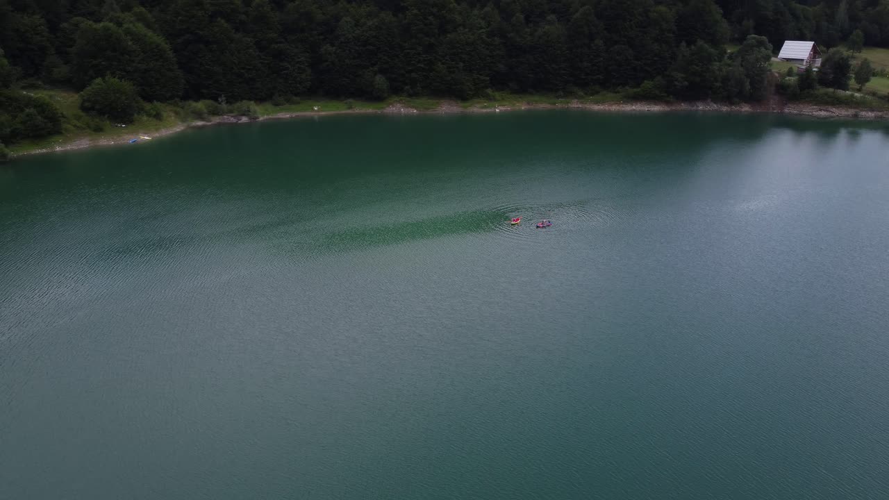 화창한 날 루마니아 도프타나 계곡의 잔잔한 호수 팔티누에서 배를 타고 즐거운 시간을 보내는 친구들의 공중 궤도 사진