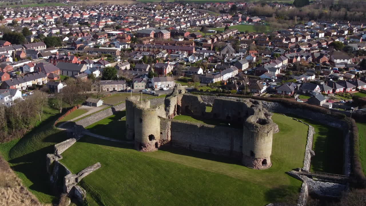 una vista aérea del castillo de rhuddlan en una soleada mañana de primavera, volando de izquierda a derecha alrededor del castillo con el zoom alejado y la ciudad de rhuddlan al fondo, denbighshire, gales, reino unido