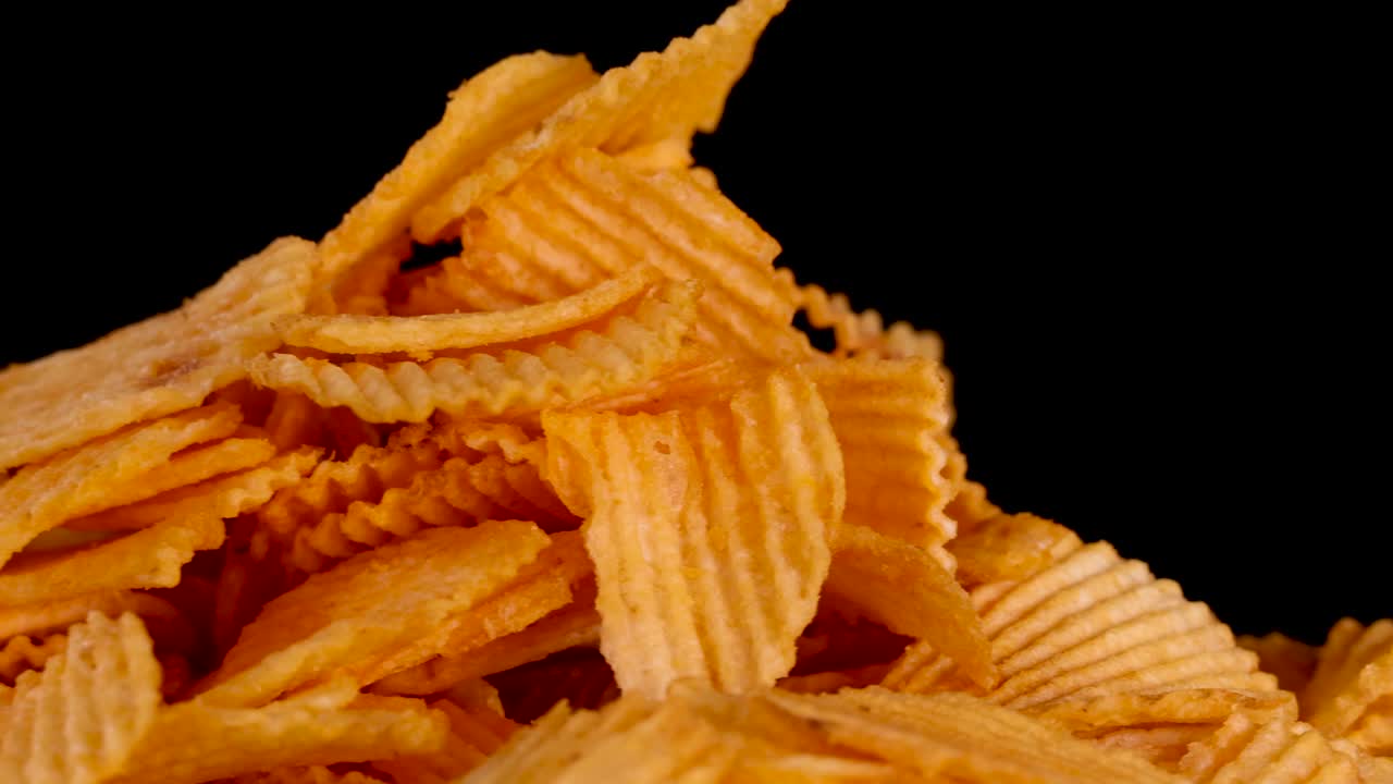 Golden ridged potato chips rotate and zoom out against black background, crisp texture highlighted