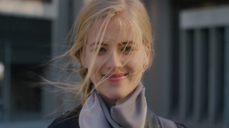 ritratto da vicino felice giovane donna bionda sorridente godendo stile di vita urbano guardando rilassato spensierato donna caucasica vento che soffia capelli slow motion