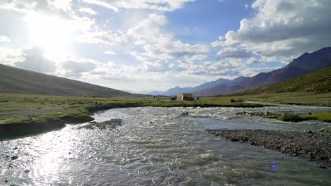 Wide-pull-back-shot-over-a-river-with-a-tent-camp-in-a-green-valley-between-mountains