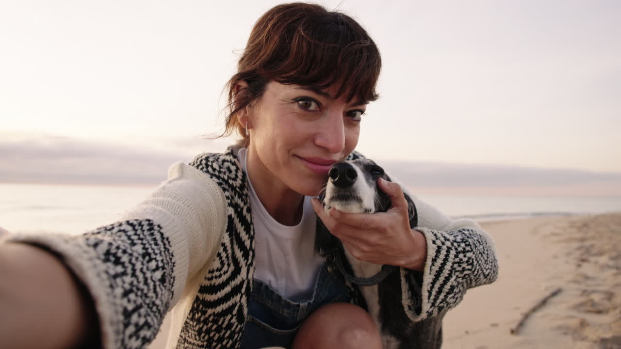 Woman taking a selfie with her dog on the beach at sunrise. Close up shot with natural light, capturing a candid lifestyle moment and connection with pet