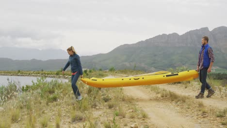 caucasian couple having a good time on a trip to the mountains, holding a kayak and walking towards