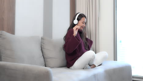 sitting on a couch in a hotel suite, a pretty young woman wearing headphones dances in place