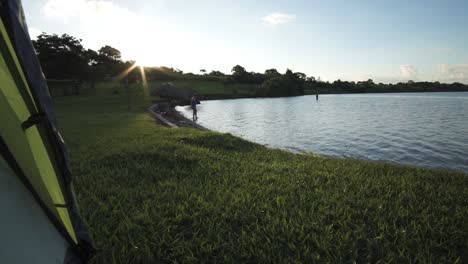 Looking-out-of-a-Tent-over-Green-Grass-and-a-Tranquil-Lake-during-Morning-Sunrise