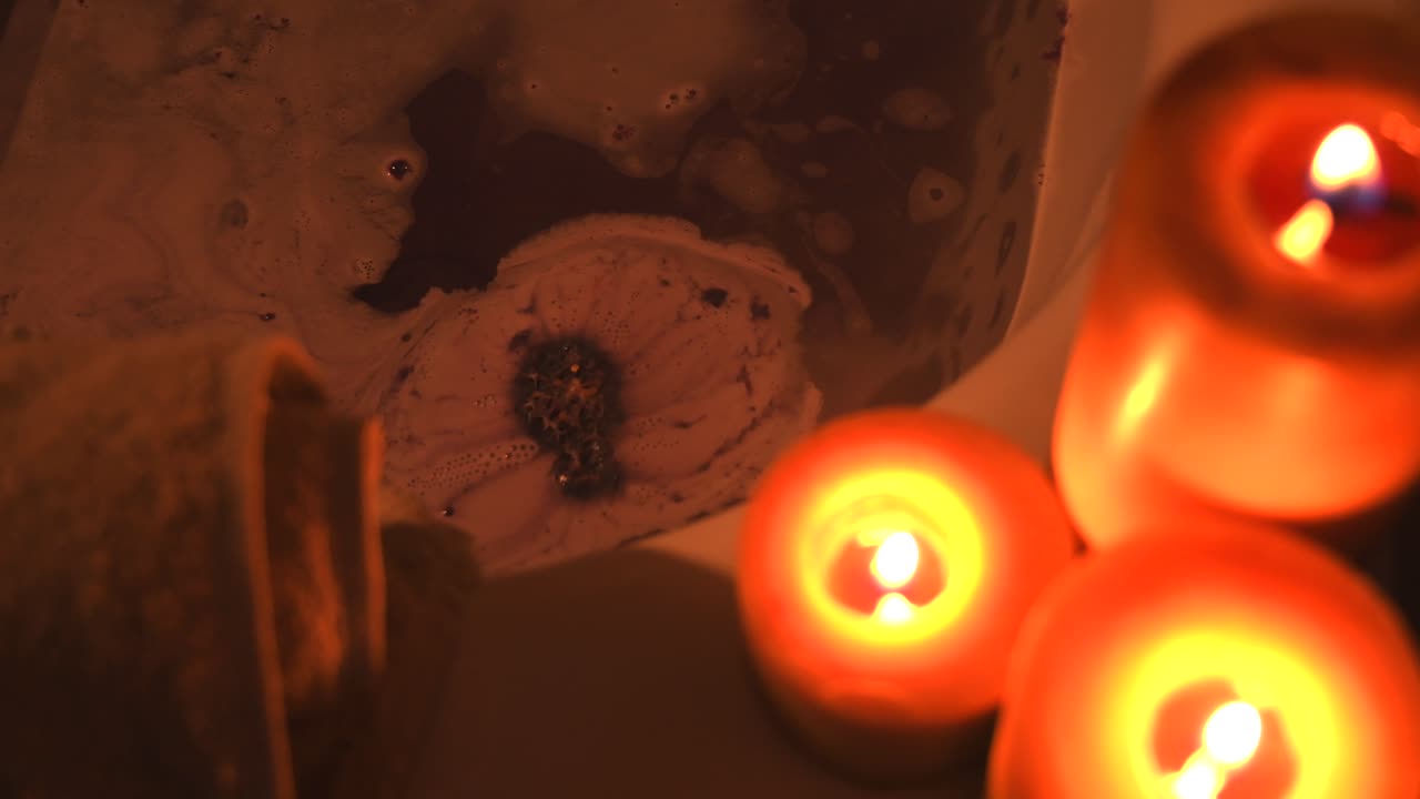 bomba de baño púrpura chisporroteando en agua caliente en una bañera, con algunas velas, haciendo burbujas y espuma