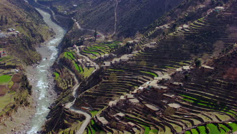 Vista-Aérea-Del-Río-De-Cachemira-Con-Un-Estilo-De-Vida-Sencillo-De-Cachemira,-Pide-Casas-Sencillas,-Con-Bordes-De-Madera,-Techos-De-Paja-Y-Pequeñas-Cabañas,-Un-Camino-Sinuoso-Con-Río-Que-Hace-Hermosas-Vistas