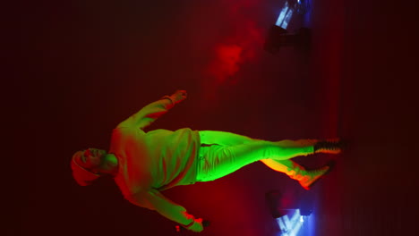 vertical video. funny male rap artist sings and dances into a microphone on a stand in the neon light of lamps and in the studio on a colorful bright background