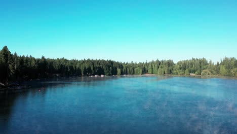 aerial pedestal above beautiful blue lake water surrounded by thick conifer tree forest