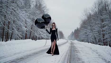 stylish woman in black dress with balloons in snowy landscape