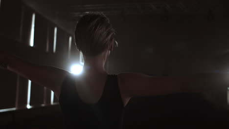 Slow-motion:-Diligent-young-graceful-ballerina-dancing-elements-of-classical-ballet-in-the-dark-with-light-and-smoke-on-the-background.-Beautiful-young-ballerina-in-darkness.