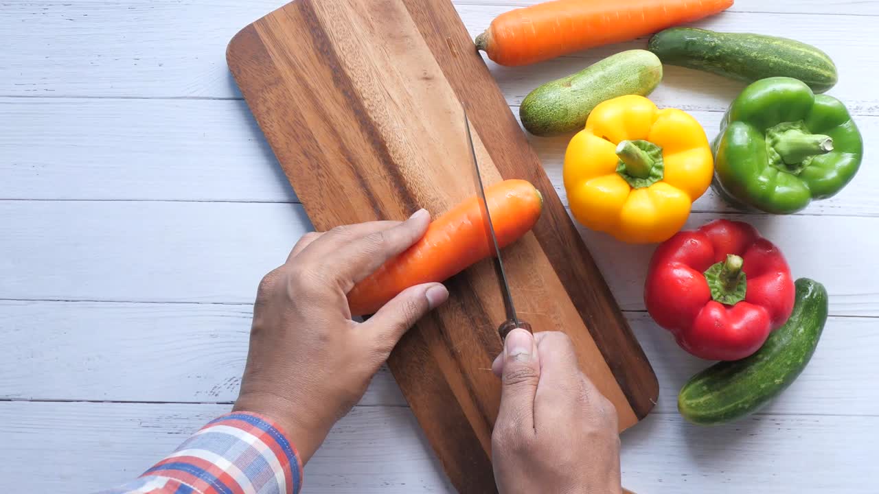vista superior de la mano del hombre cortando zanahorias frescas en la tabla de cortar en la mesa