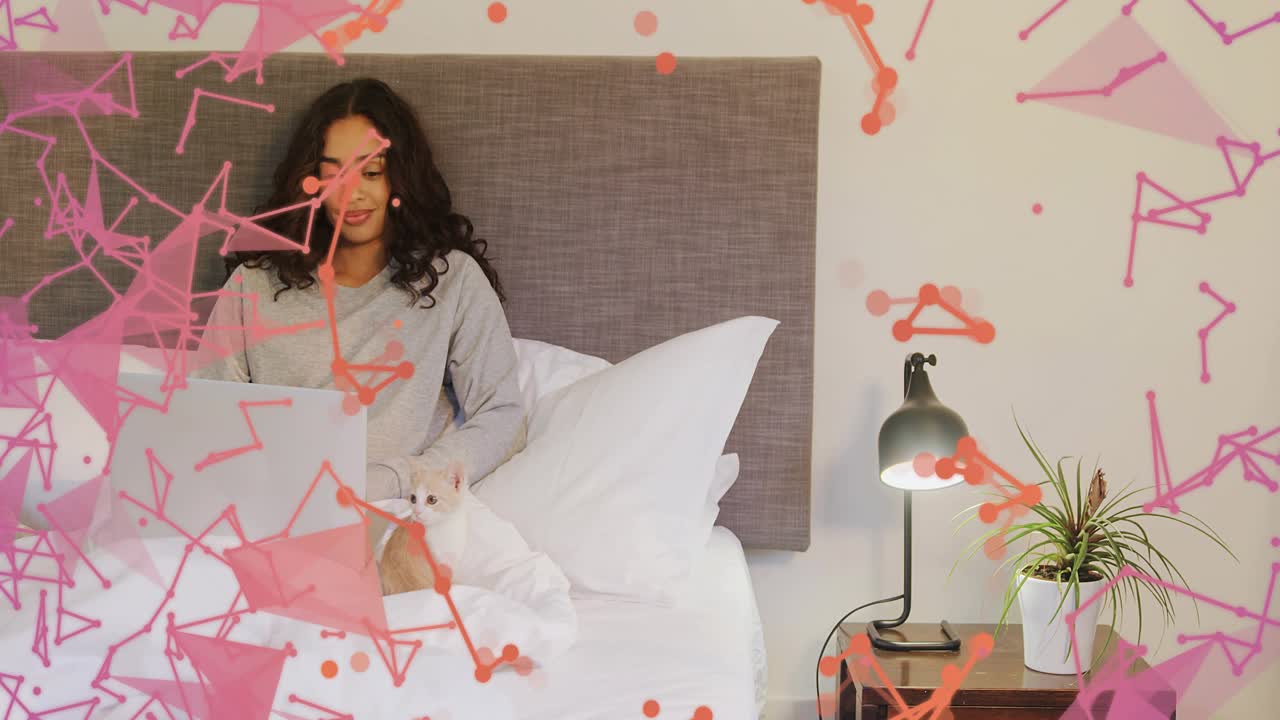 Woman typing on laptop in bed, cat near her, causing particles animating across front, showing tech