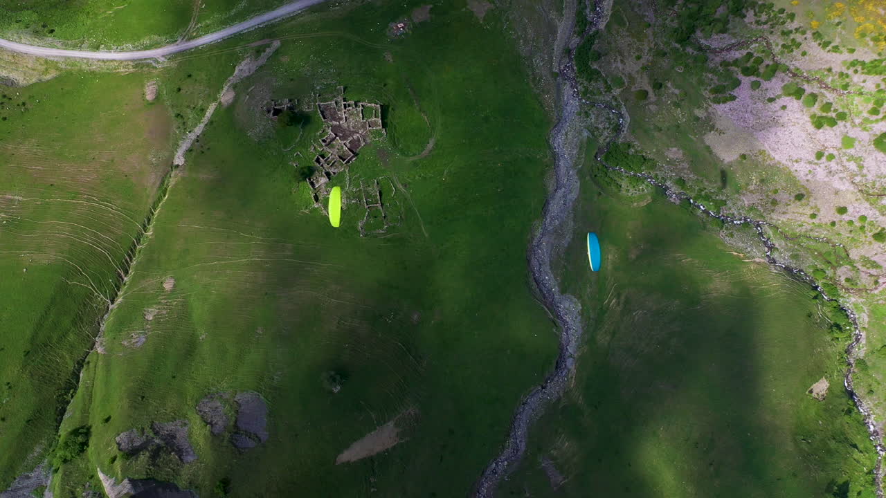 조지아 구다우리 산골짜기에서 비행하는 두 패러글라이더의 아래쪽 각도 드론 샷