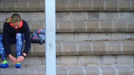 Front-view-of-young-Caucasian-female-athlete-tying-shoes-at-sport-venue-4k