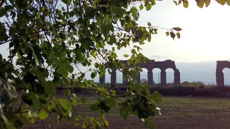 An-aqueduct-from-ancient-Rome-in-parco-degli-acquedotti-in-the-outskirts-of-the-capital-of-Italy-with-tree-leaves-in-the-foreground,-static-shot-and-slow-motion