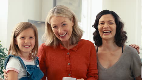 portrait of multi-generation female family with same sex partner sitting in kitchen at home talking