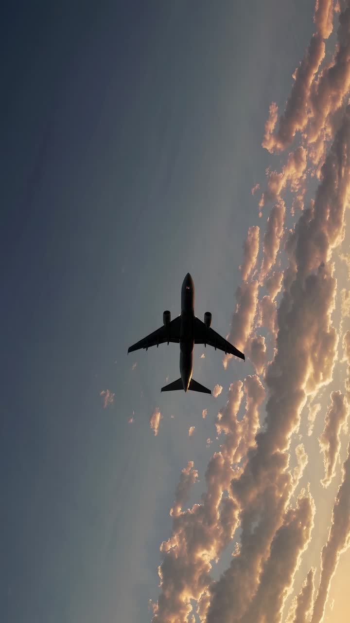 Aerial video shot of an airplane silhouetted against a dramatic sunset sky, with clouds