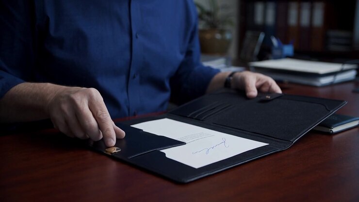 Close-up of hands closing a black document folder on a wooden office desk at the end of a meeting