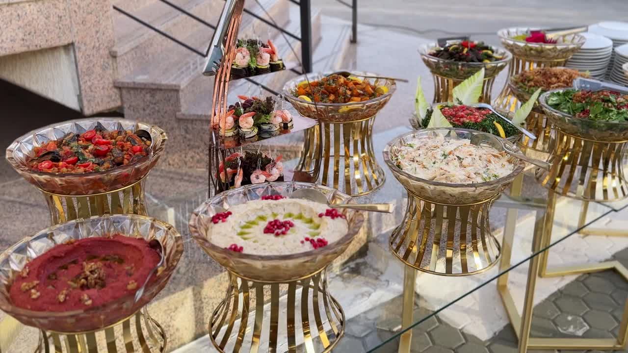 Elegante tavolo da catering all'aperto con mezze arabi, insalate fresche e tartine di gamberi su supporti dorati, ideale per matrimoni, eventi aziendali, Ramadan iftar e banchetti