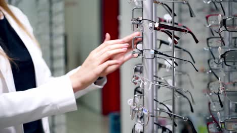 customer choosing new glasses in the store of eyewear. young woman turning stand with fashionable spectacles at optics. eyeglasses choice.
