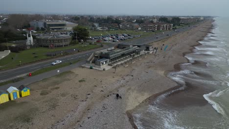 overcast day on a pebble beach in brighton, uk. gentle waves wash the shore. colorful beach huts line the beach next to a road.