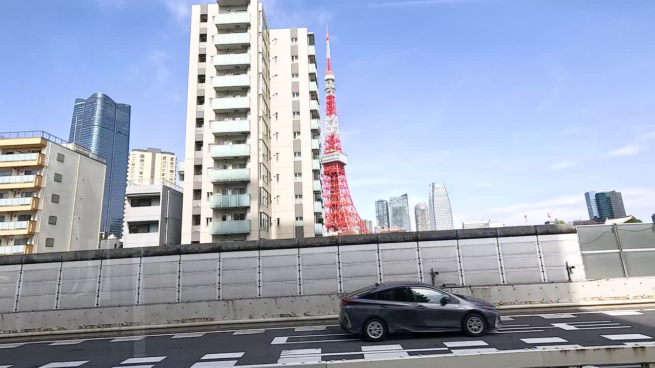 Vehicles move along a Tokyo street with Tokyo Tower in the background under clear blue skies
