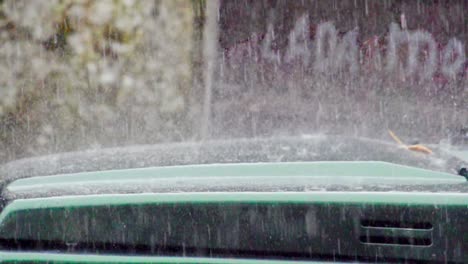 torrential rain splashing off the hood of a parked green car