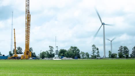 Zeitraffer-Vom-Bau-Einer-Windmühle,-Während-Sich-Im-Hintergrund-Windmühlen-Im-Wind-Drehen