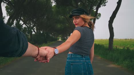 4K-UHD-Cinemagraph-of-a-young-brunette-woman-with-a-watch-standing-in-an-alley-of-pine-trees-in-Tuscany,-Italy-holding-hands