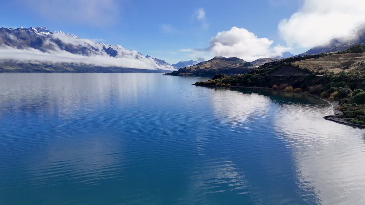 Drone footage captures tranquil Lake Wakatipu with surrounding mountains and clouds, showcasing New Zealand's natural beauty