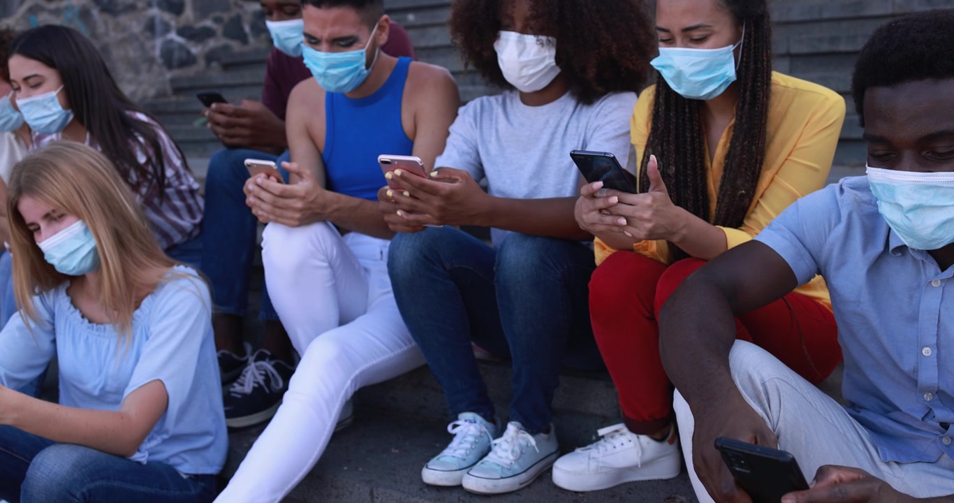 Giovani di diverse etnie con mascherine che usano gli smartphone all'aperto