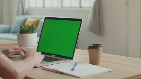 close up man uses laptop with green mock-up screen while sitting at the desk in his living room, video in 4k