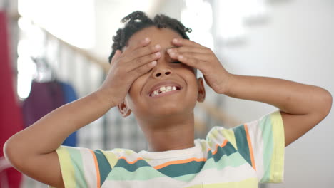 african american boy covers his eyes with his hands, smiling broadly at home