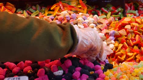 a hand in a glove reaching into a bin of colorful candies.