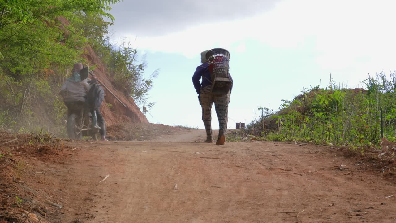 Abitanti del villaggio a piedi e in motorino che salgono una collina su una strada sterrata polverosa, Vietnam, Kon Plong.