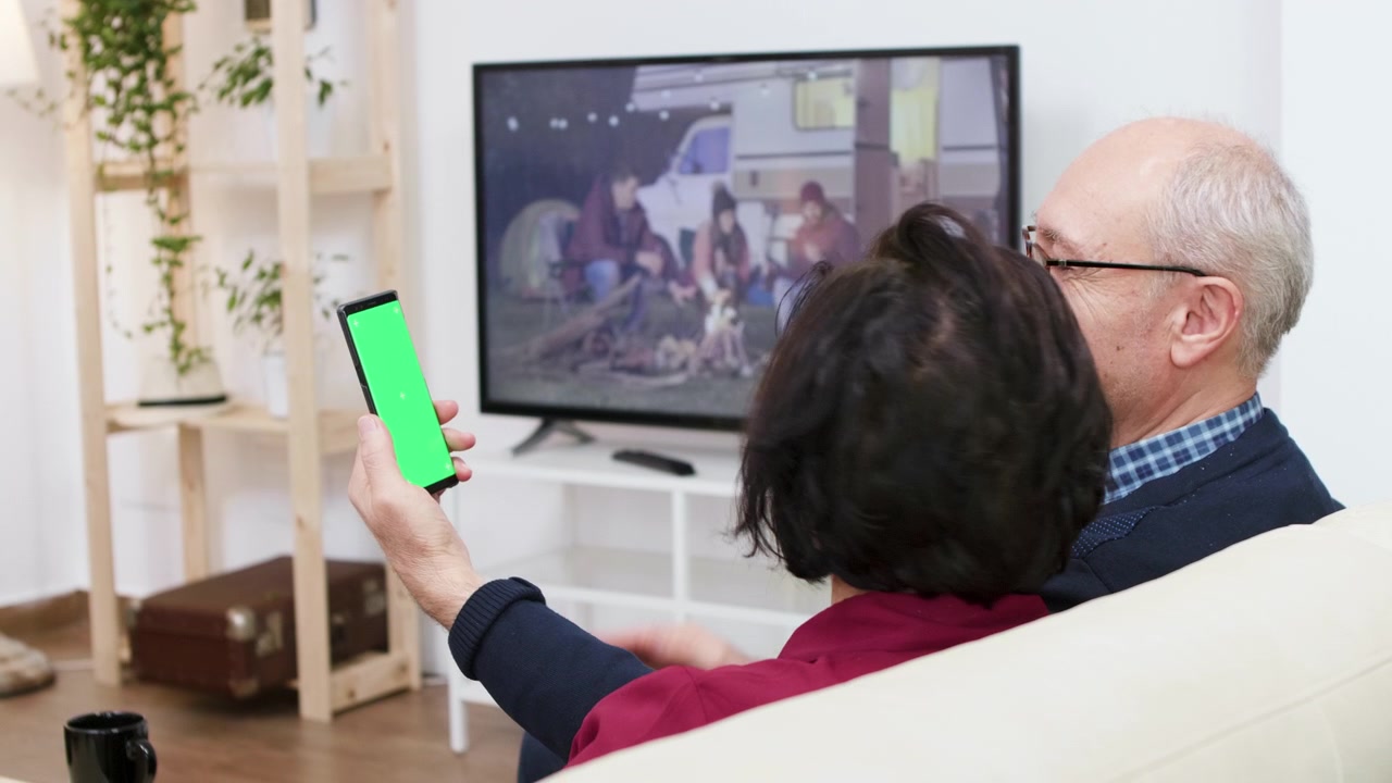 Coppia anziana che guarda la televisione e usa lo smartphone a casa