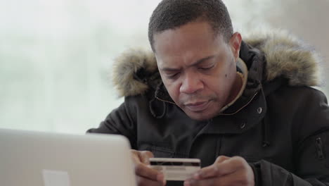 afro-american middle-aged man in black jacket with fur hood sitting outside