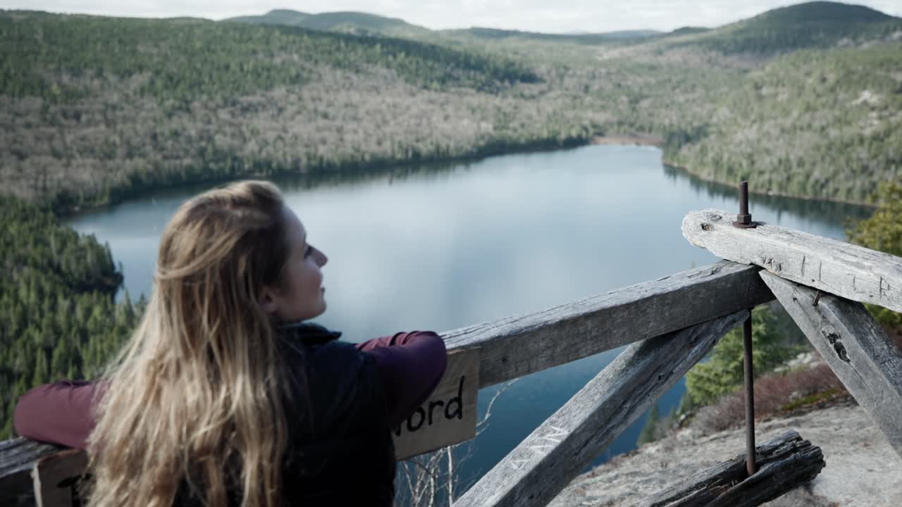 mujer viajera admirando el hermoso paisaje del lago tranquilo y el denso bosque desde una plataforma de observación de madera en saint-come, quebec, canadá