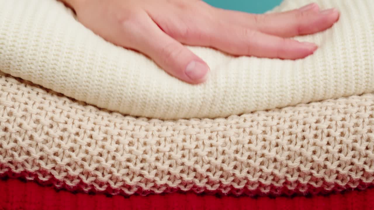 Woman's hand holding a stack of knitted sweaters