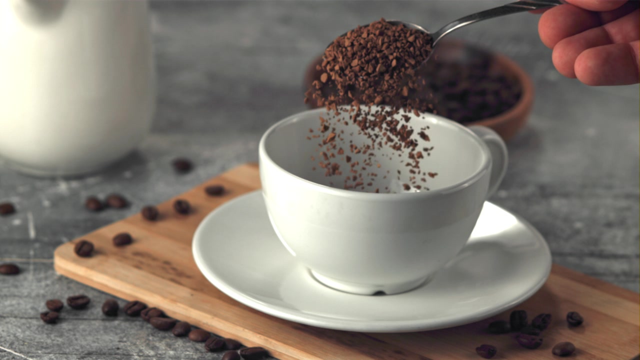 Heller instant kaffegranulat ned i en hvit kopp i sakte film