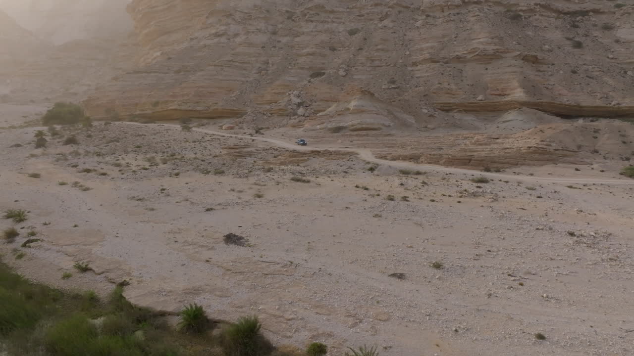 Aerial shot of a vehicle on a dusty trail in a desert oasis near the coast of Oman